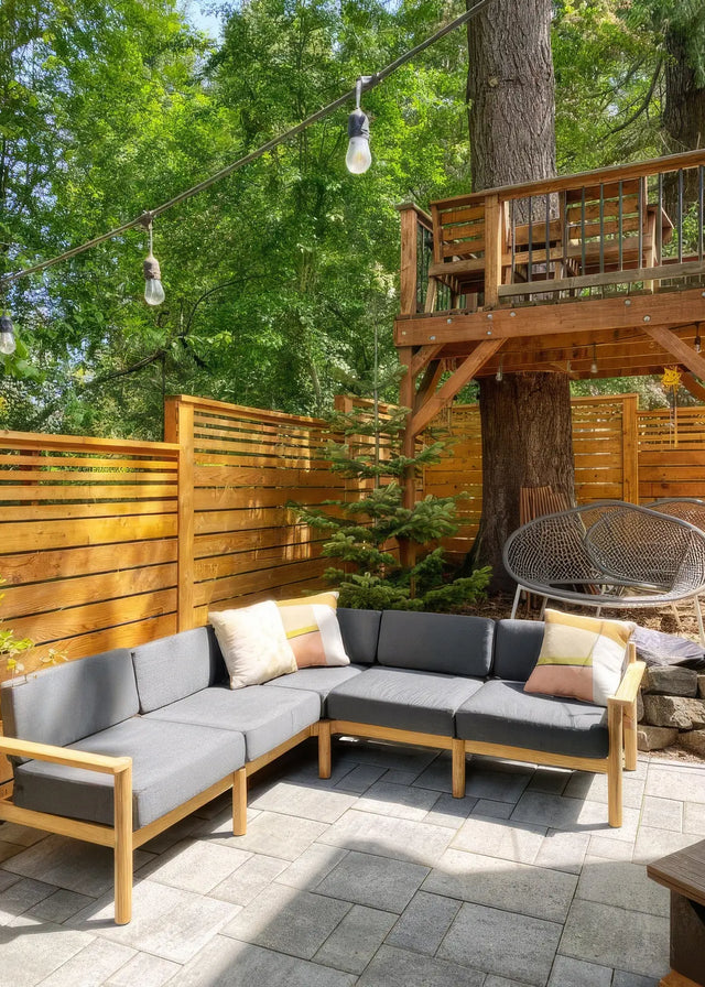 Customer photo - Neighbor outdoor sectional in dark charcoal on a stone patio with colorful throw pillows, string lights and treehouse behind